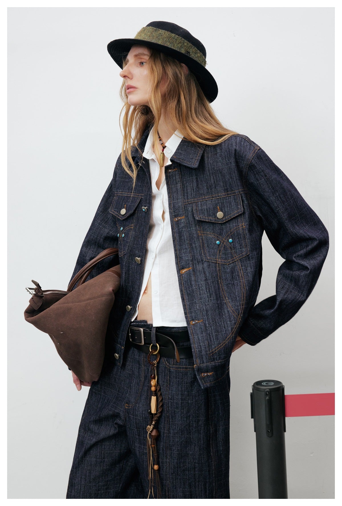 Model wearing an open dark indigo jacket with decorative stitching over a white shirt and matching trousers.