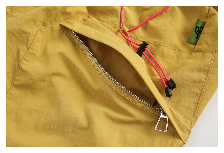 Close-up of a zippered pocket on mustard shorts, with pink drawcords and a small woven tag.
