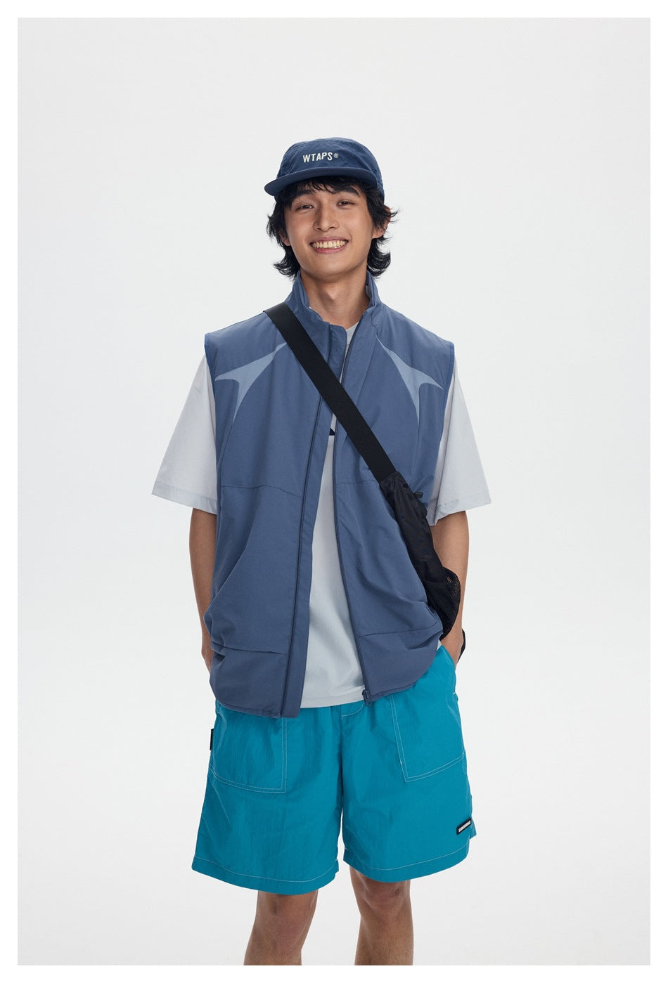 Front view of a model wearing a blue-gray patterned sleeveless vest over a white T-shirt with turquoise shorts.