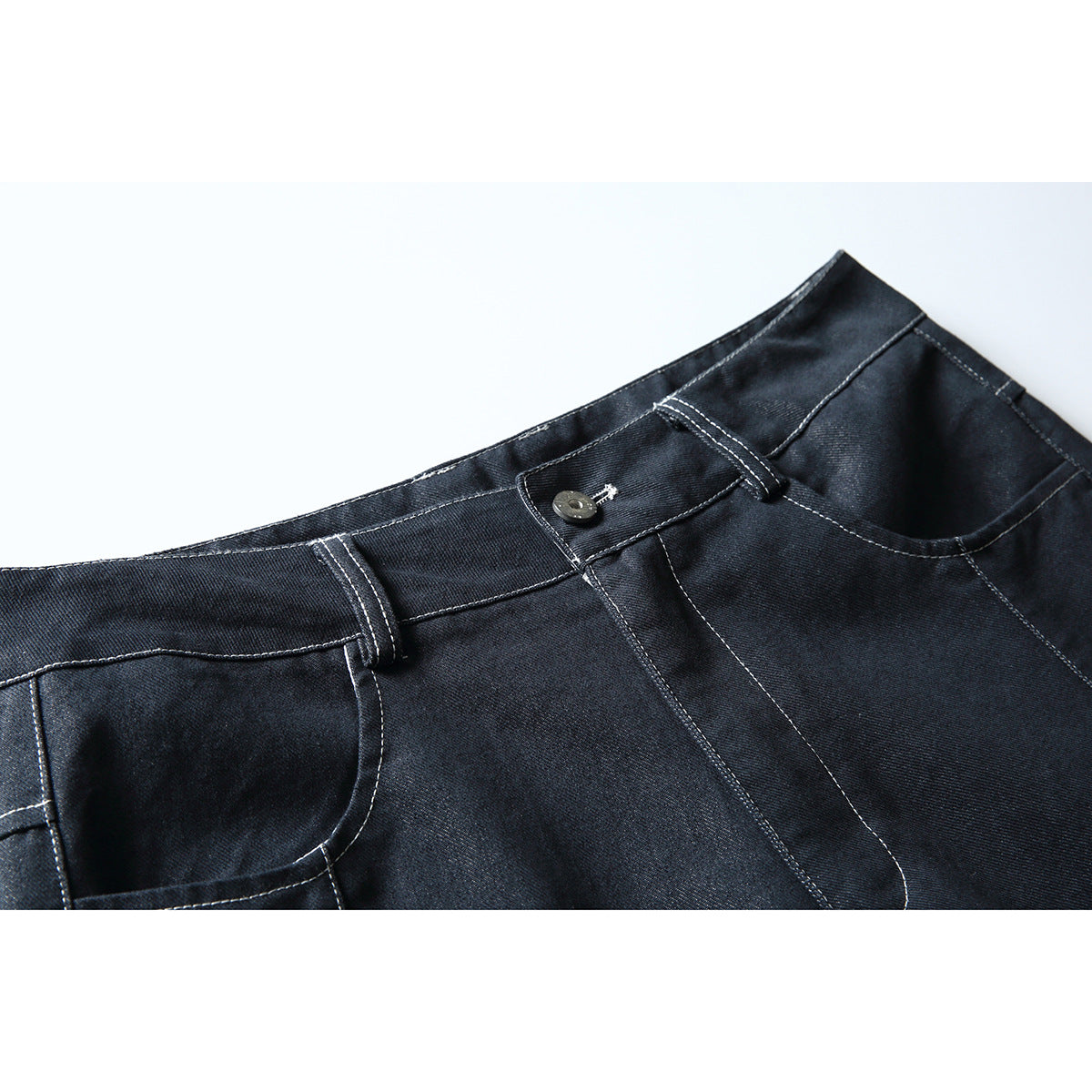 Close-up of dark indigo trousers showing the waistband, button, belt loops, and curved front pockets with contrast stitching.