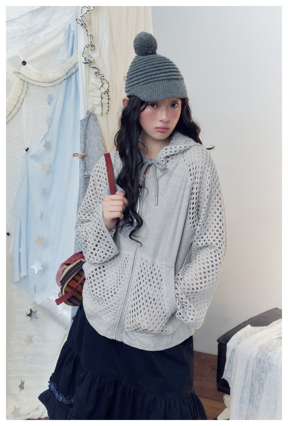 Model wearing a light gray zip-up hoodie with open-knit mesh sleeves and pockets, paired with a black skirt.