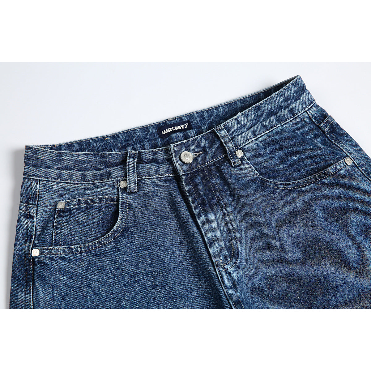 Close-up of the front waistband and pockets of blue washed jeans, with a button and belt loops.
