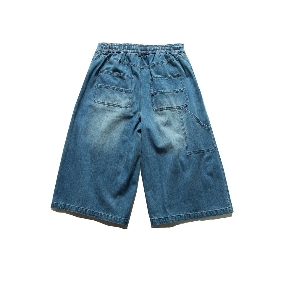 Back view of blue washed denim shorts with elastic waistband, patch pockets and side carpenter panel