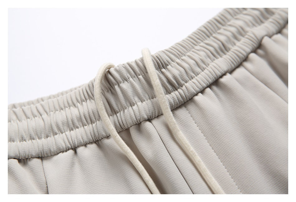 Close-up of gathered waistband and cream drawstrings on light beige joggers.