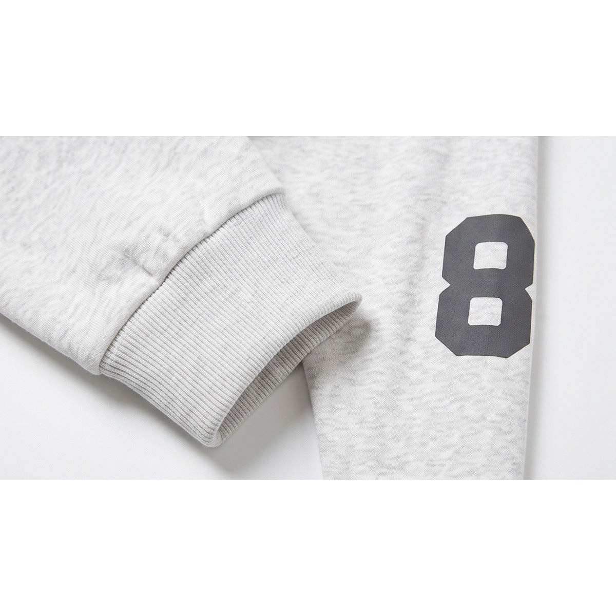 Close-up of a ribbed cuff and dark number 8 printed on a light gray marled sweatshirt sleeve.