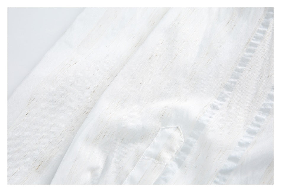 Close-up of a small stitched fabric tab beside a seam on the white shirt, with subtle tan streaks and pale blue accents.