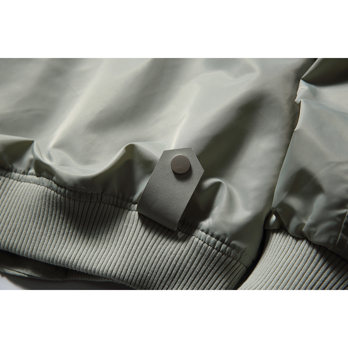 Close-up of the pale gray bomber jacket's ribbed hem and snap-tab detail.