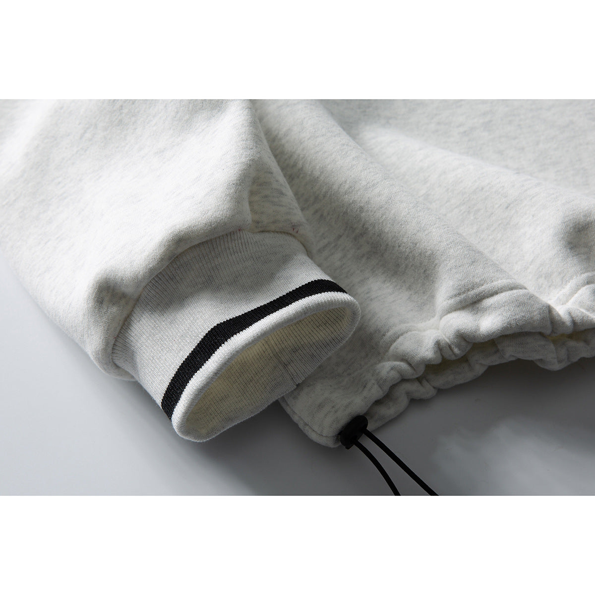 Close-up of a light gray sweatshirt sleeve cuff with a narrow black stripe, gathered hem, and drawcord.