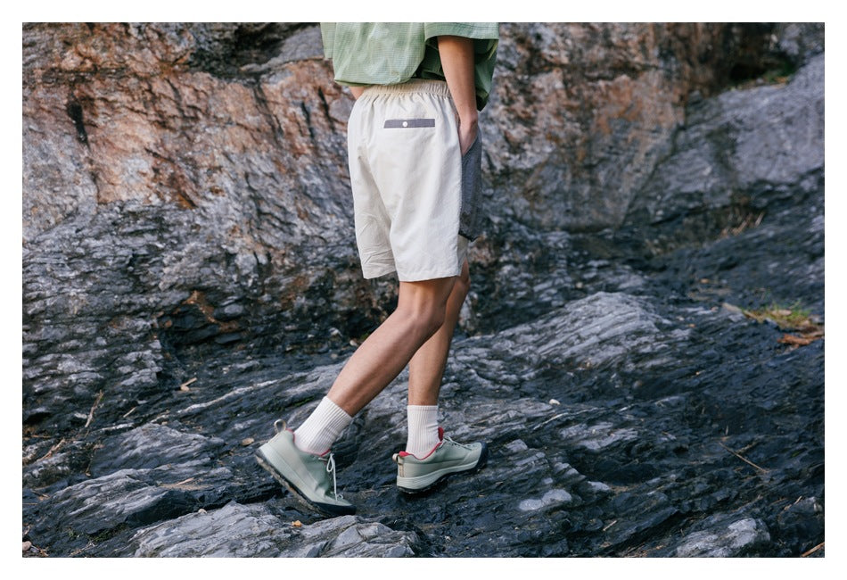 Rear three-quarter view of ivory shorts with a small gray buttoned back pocket, worn on rocky terrain.