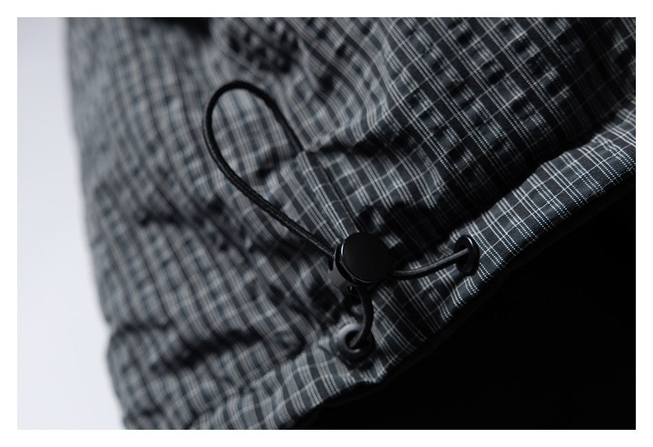 Close-up of a black adjustable drawcord toggle on dark gray plaid fabric.