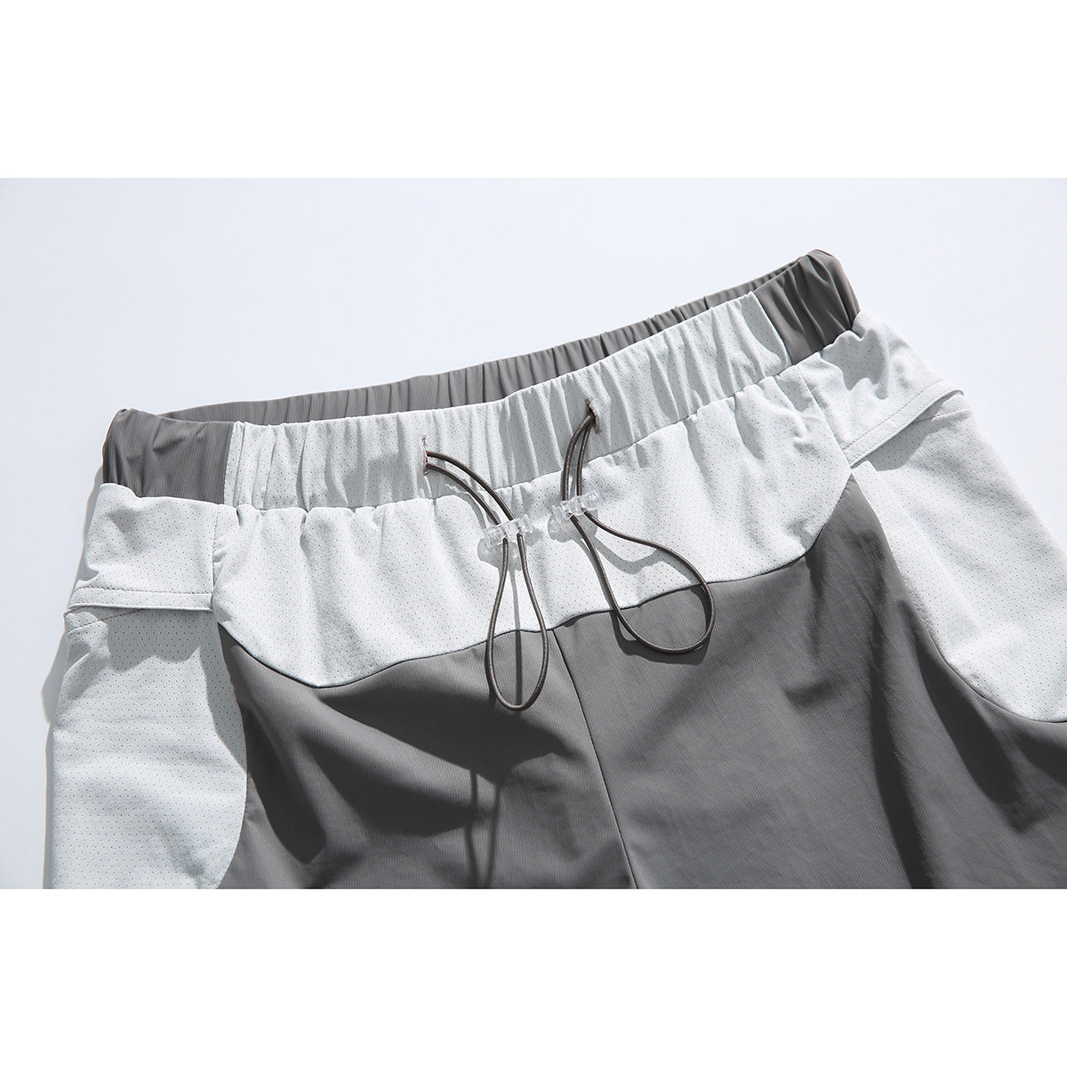 Close-up of gray shorts with a white perforated waistband panel, elastic waist, and adjustable drawcords.