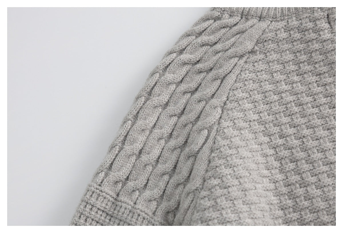 Close-up of a light gray sweater sleeve with cable-knit panels and a ribbed cuff.