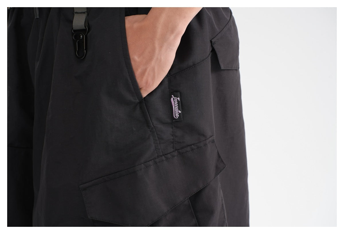 Close-up of black cargo pants showing a side pocket, flap cargo pocket, small sewn label, and clip strap.