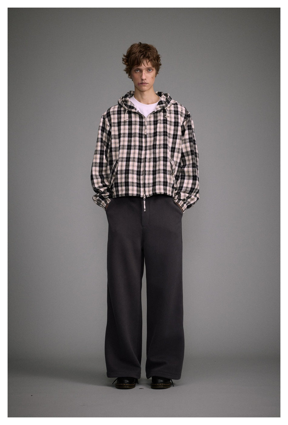 Full-length view of a model wearing a black and pale pink plaid hooded jacket and black wide-leg trousers.