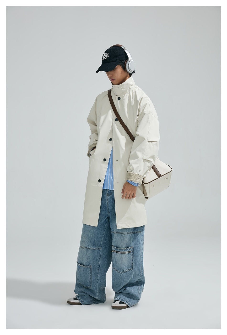 Person wearing an ivory button-front coat with checked cuffs and loose blue jeans.