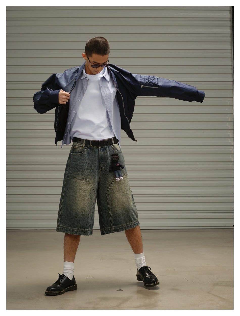 Model wearing an open navy jacket over a pale shirt and white tee with oversized faded denim shorts.