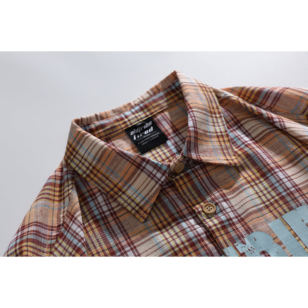 Close-up of a tan, rust, cream and blue plaid shirt collar, buttons and inner neck label.