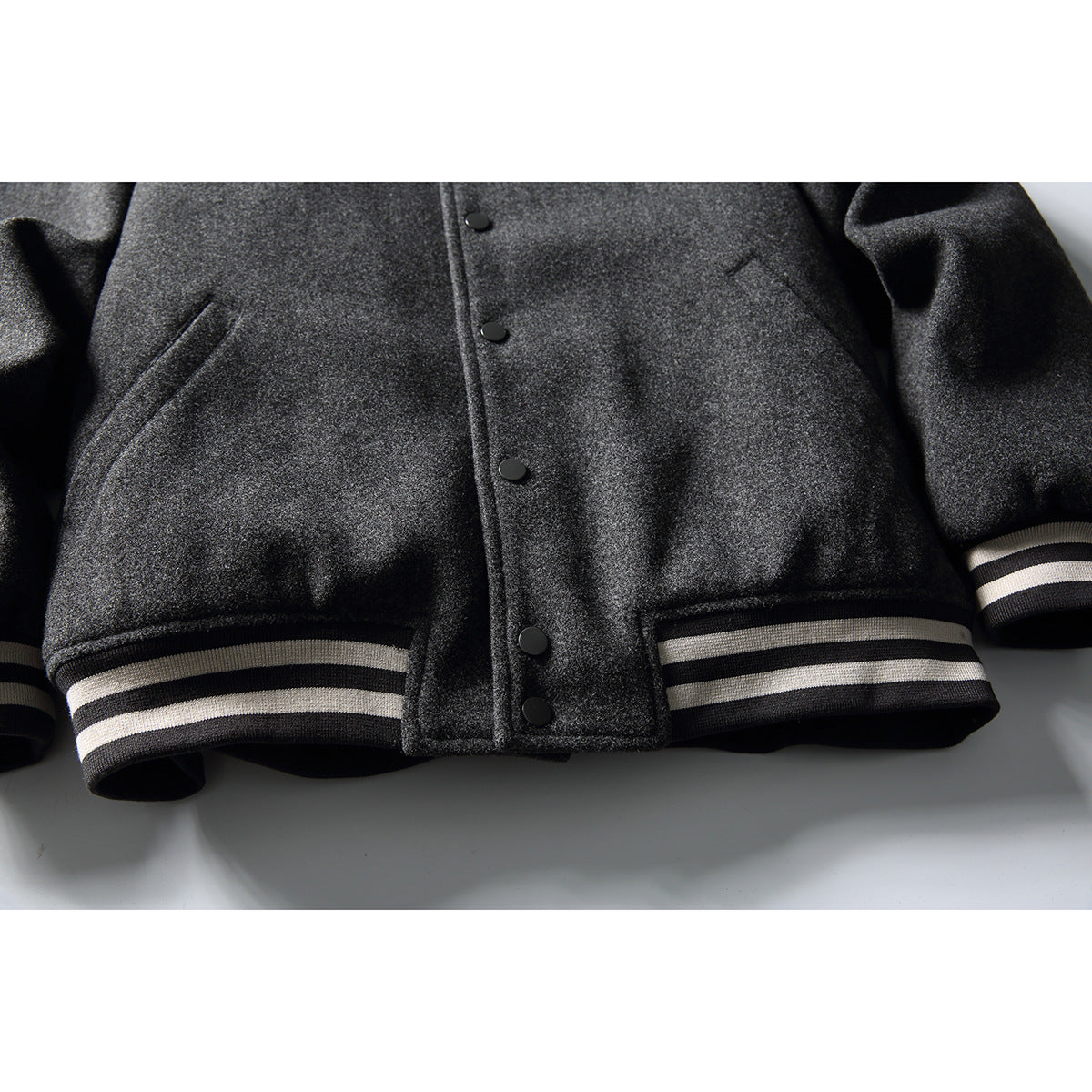 Close-up of a charcoal gray jacket front with black snaps, angled pockets, and striped ribbed hem and cuffs.
