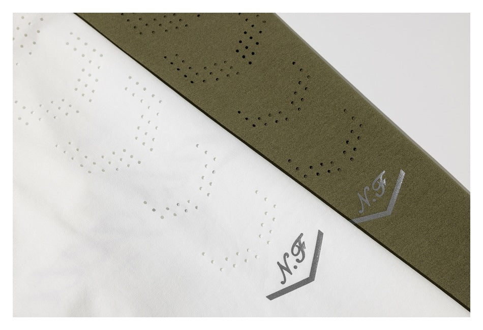 Close-up of white and olive-green shirts showing dotted perforation patterns and small gray printed motifs.