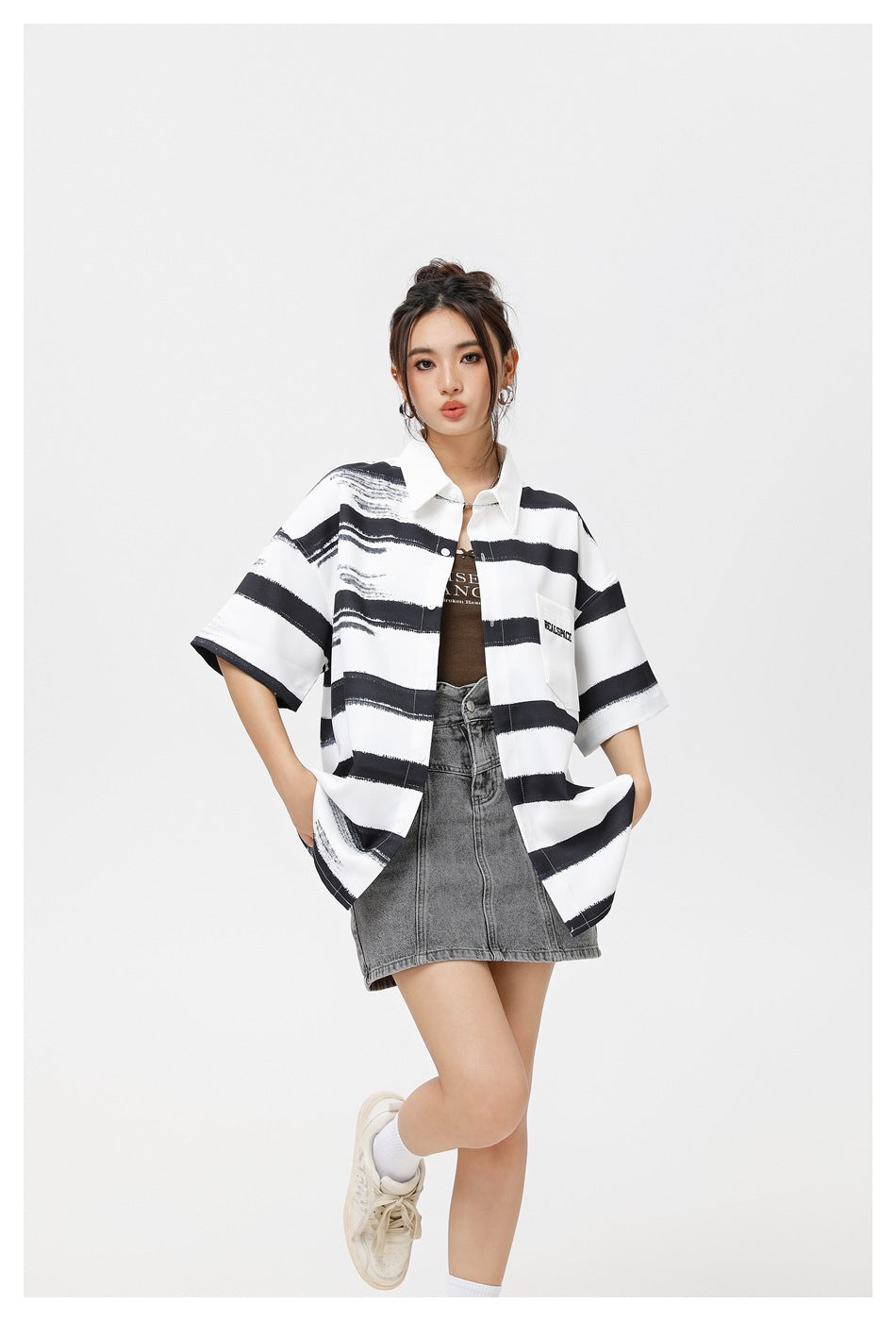 Closer view of a model wearing an oversized white shirt with black brushstroke stripes over a gray denim mini skirt.