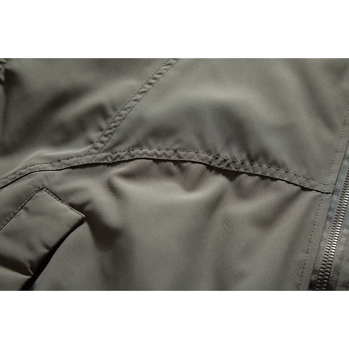 Close-up of dark olive-gray jacket fabric, curved stitching, and a section of the zipper.