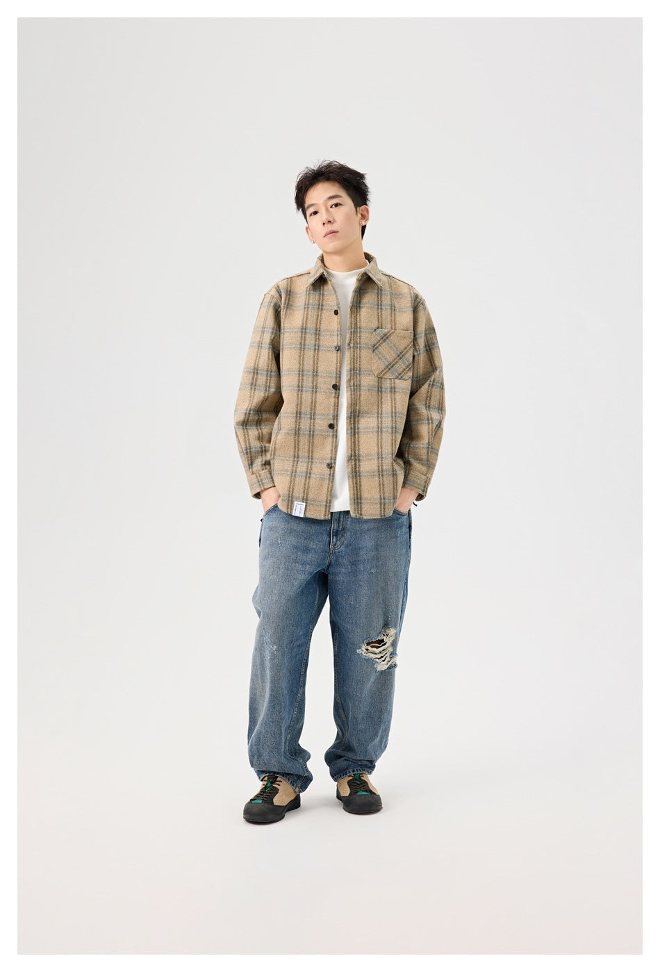 Model wearing a light khaki plaid button-up shirt open over a white tee with blue jeans, full-length view
