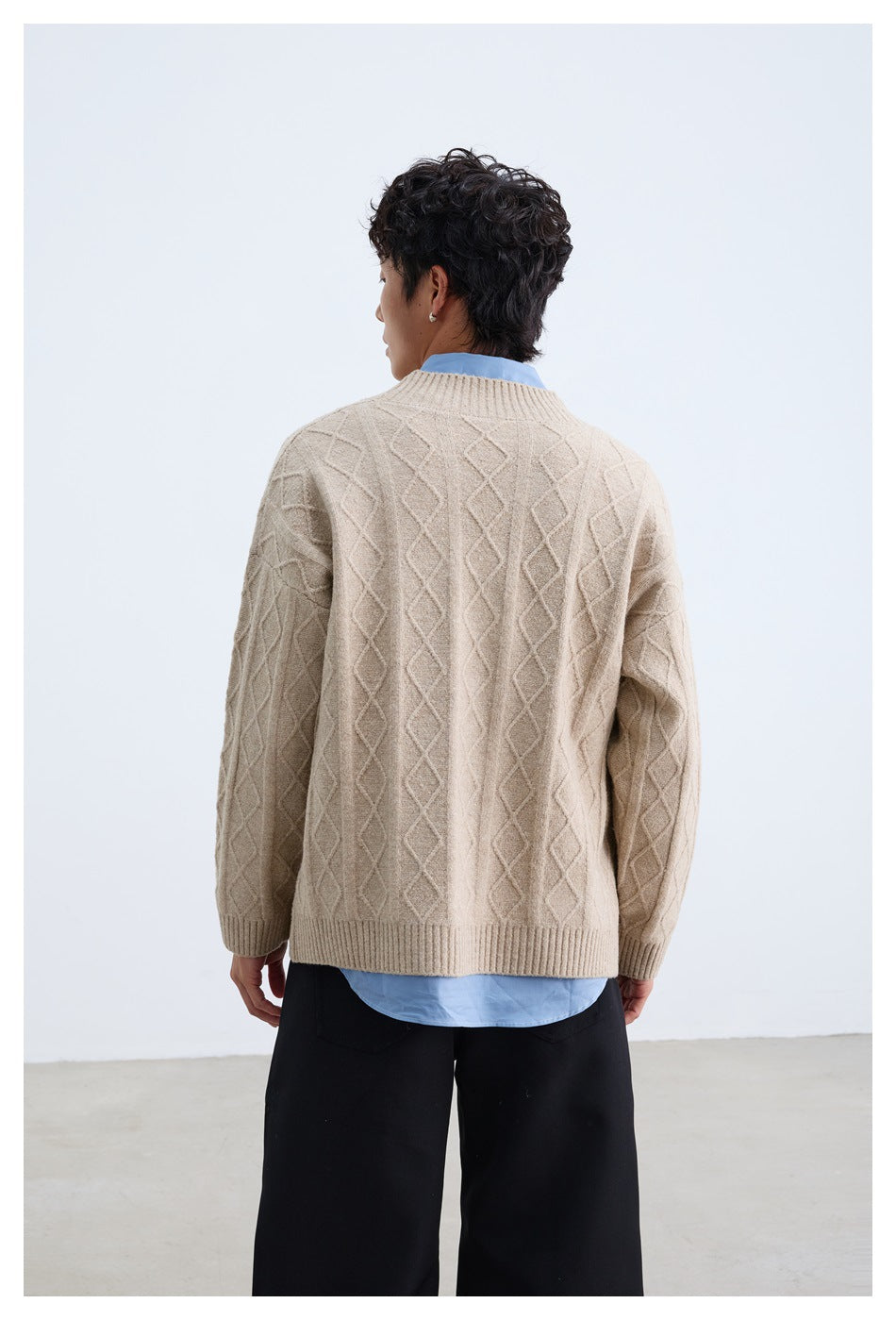 Rear view of a model wearing a beige diamond cable-knit cardigan with ribbed cuffs and hem.