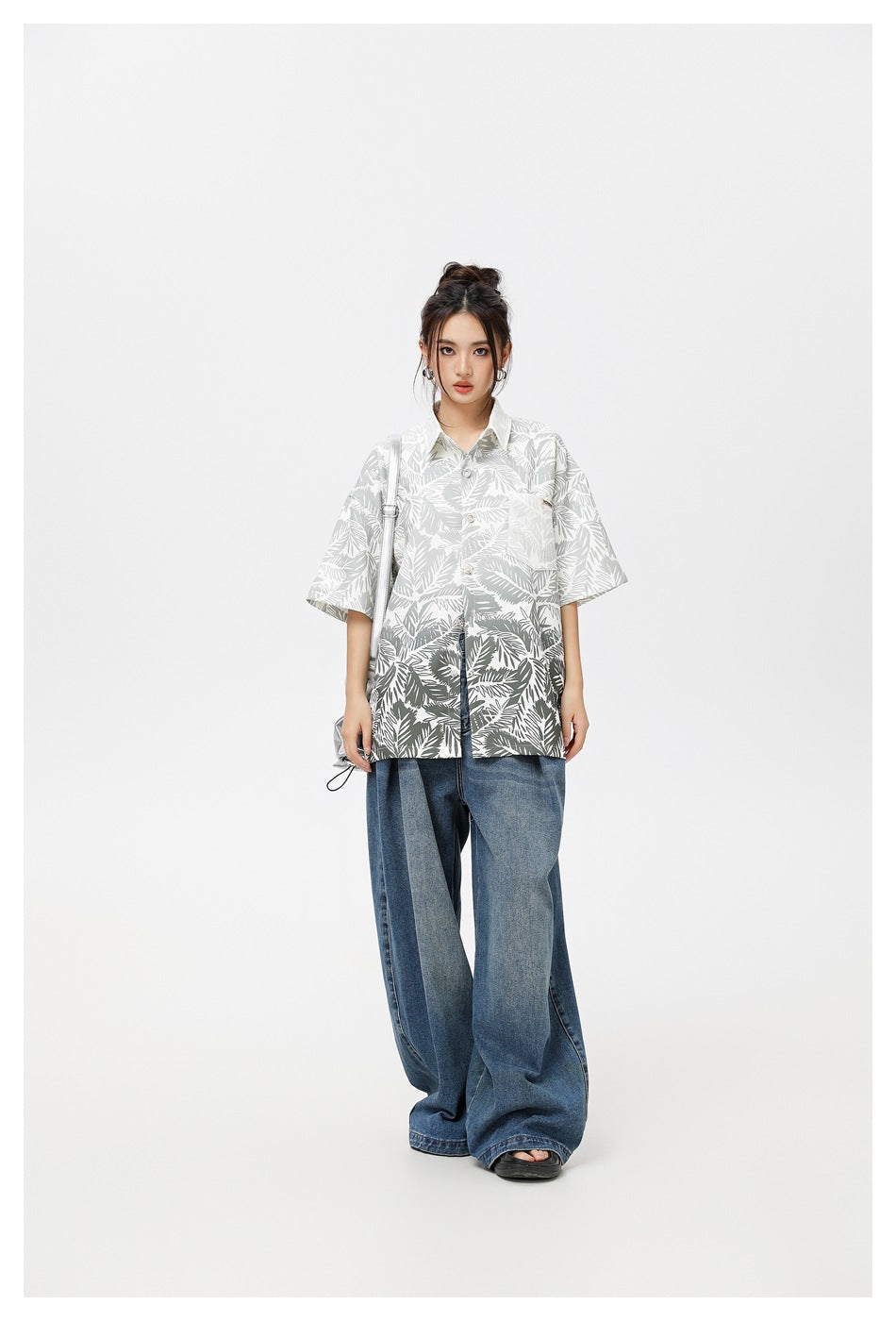 Full-length view of a woman in the gray leaf-print oversized short-sleeve shirt with wide-leg jeans