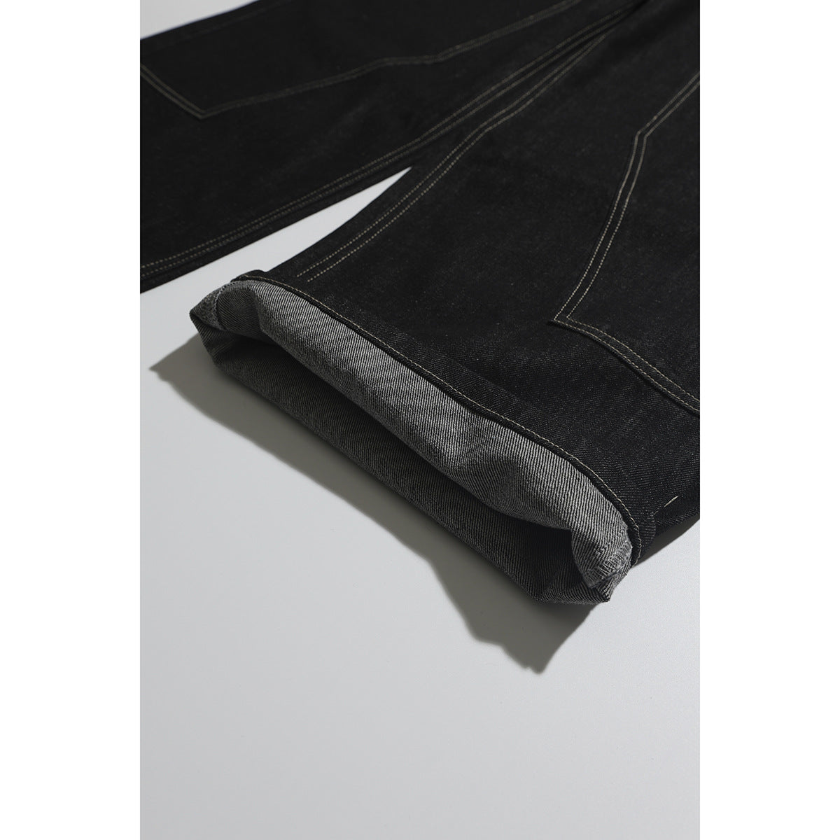 Close-up of black jeans with a turned-up hem revealing the lighter reverse side of the denim.