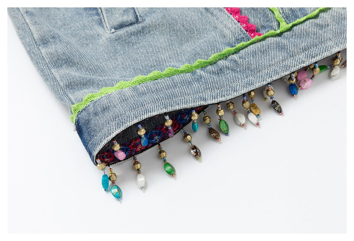 Close-up of a light blue denim edge with green trim, colorful embroidery and dangling multicolored beads.