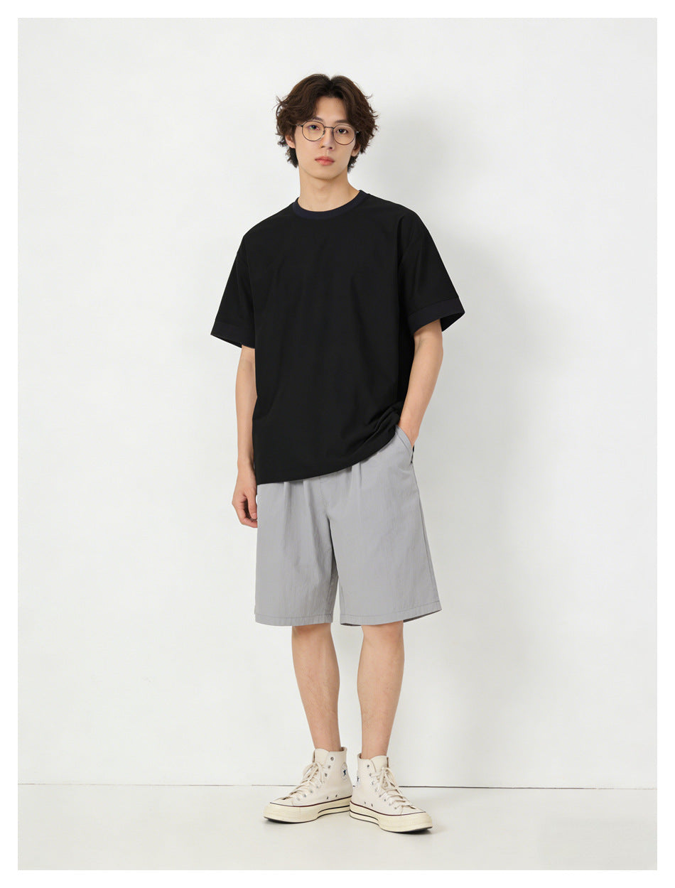 Model wearing a black relaxed short-sleeve t-shirt with gray shorts and cream high-top sneakers, front view