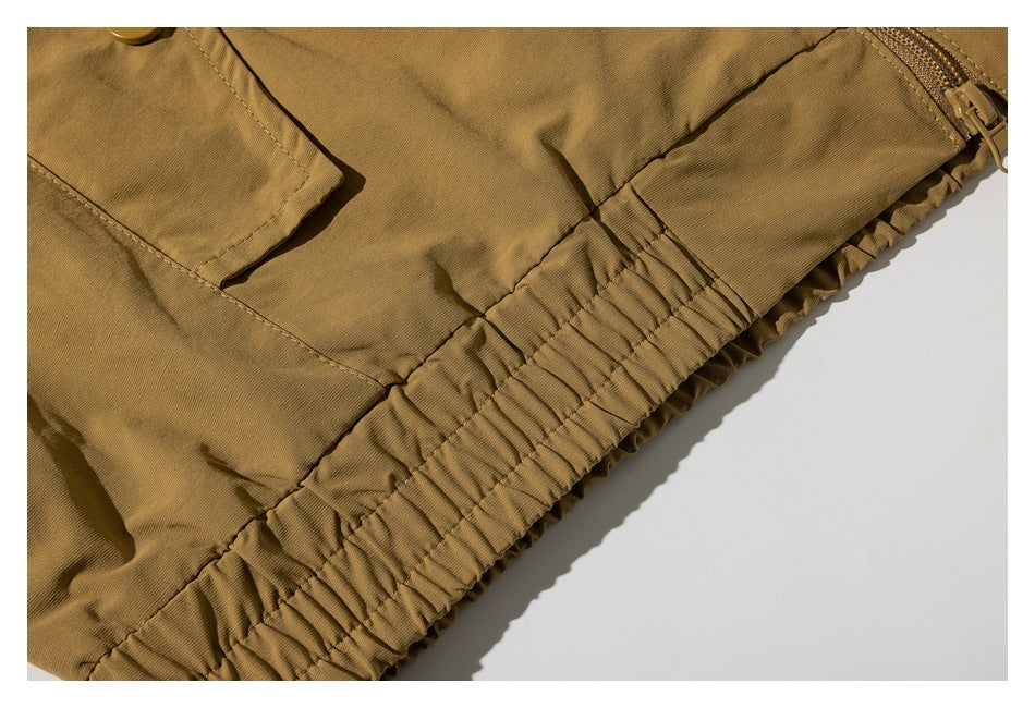 Close-up of a mustard-brown garment with a gathered elastic hem, pocket flap, and zipper.