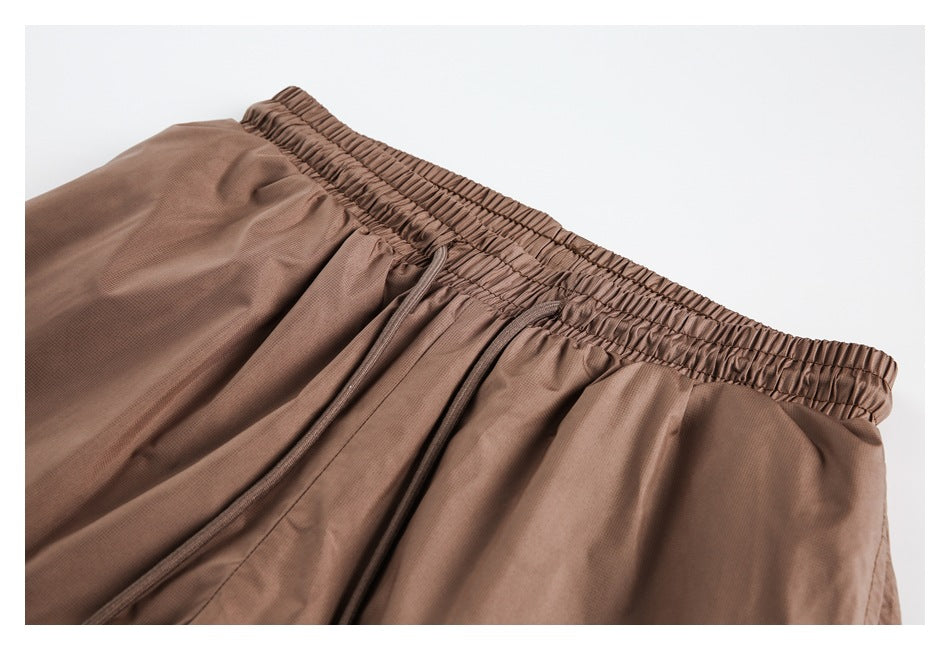 Close-up of brown shorts showing the gathered elastic waistband, matching drawstring, and stitching.