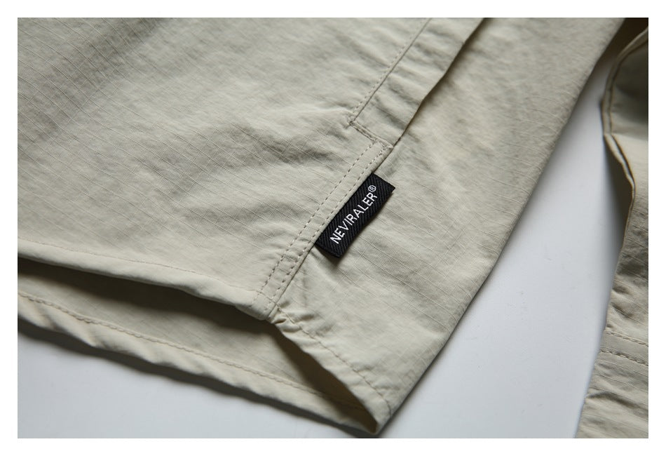Close-up of a stitched side seam and small black brand tab on the light beige shirt.