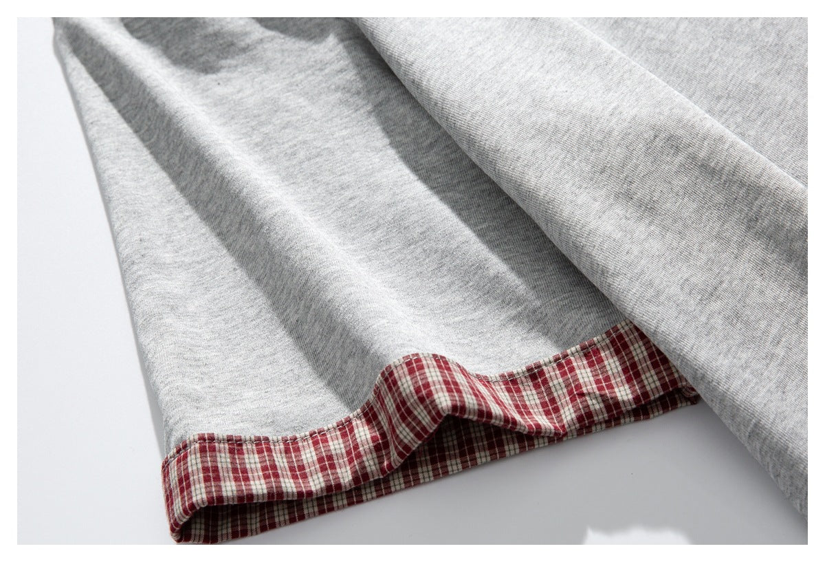 Close-up of a light gray shirt hem with red-and-white plaid fabric visible on the inside.