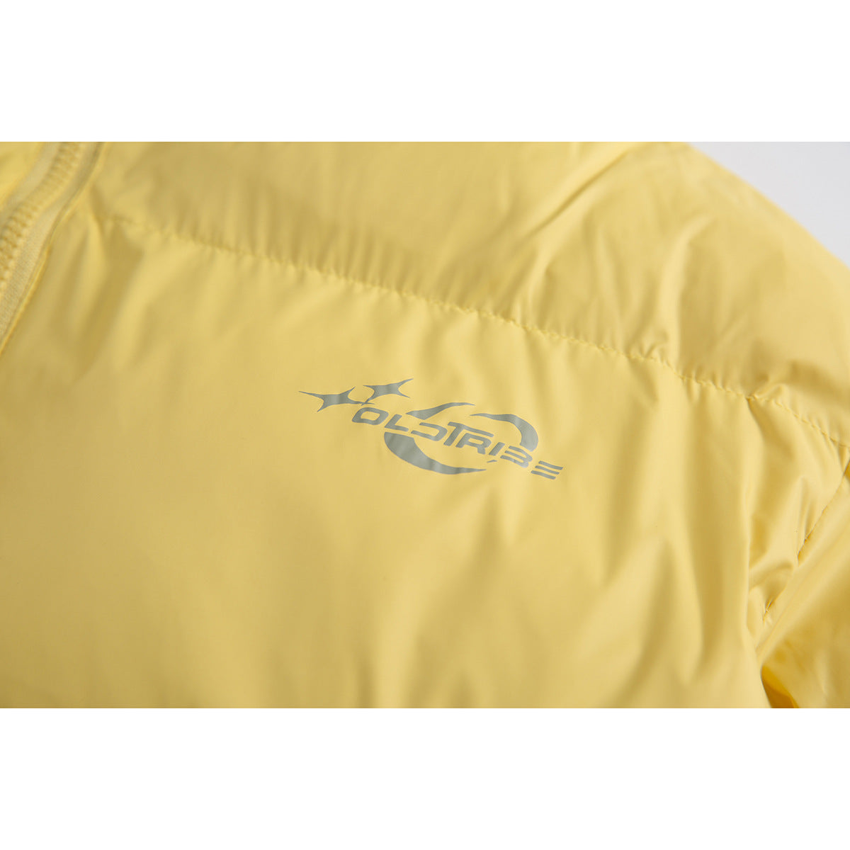 Close-up of a small gray stylized logo on the chest of a yellow puffer jacket.