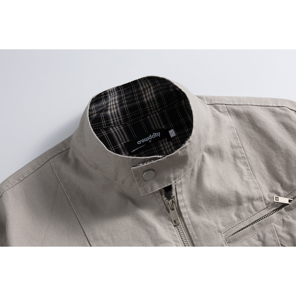 Close-up of a light gray jacket's stand collar, center zipper, chest pocket, and plaid inner label.