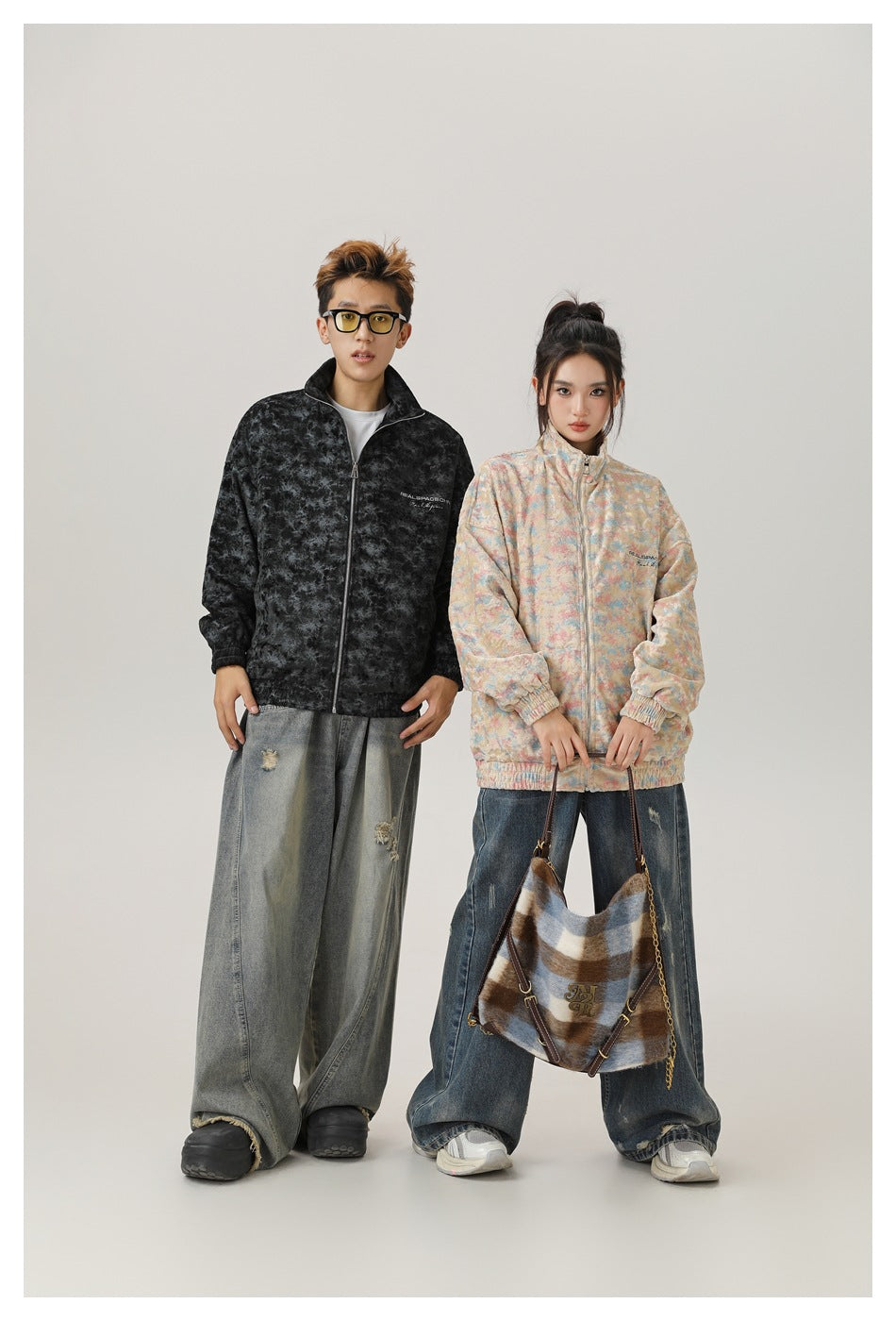 Man in black textured zip jacket with wide-leg jeans, standing beside a woman in the beige multicolor version