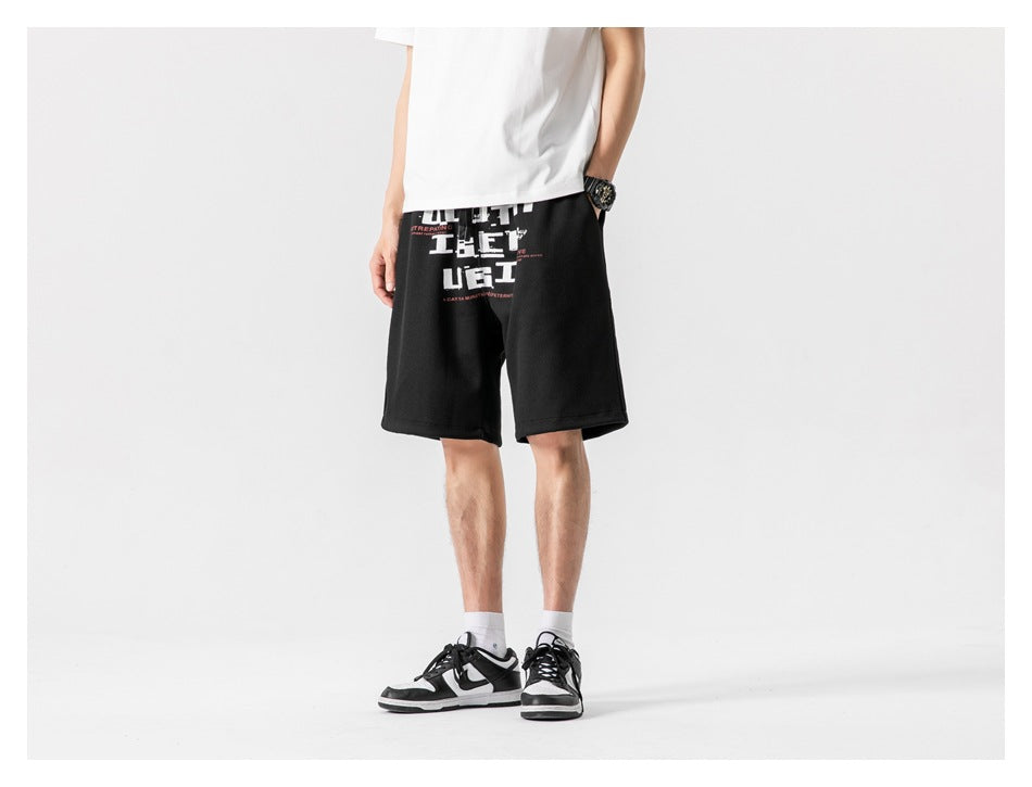 Slightly angled front view of a model wearing black knee-length shorts with a white and red graphic print.