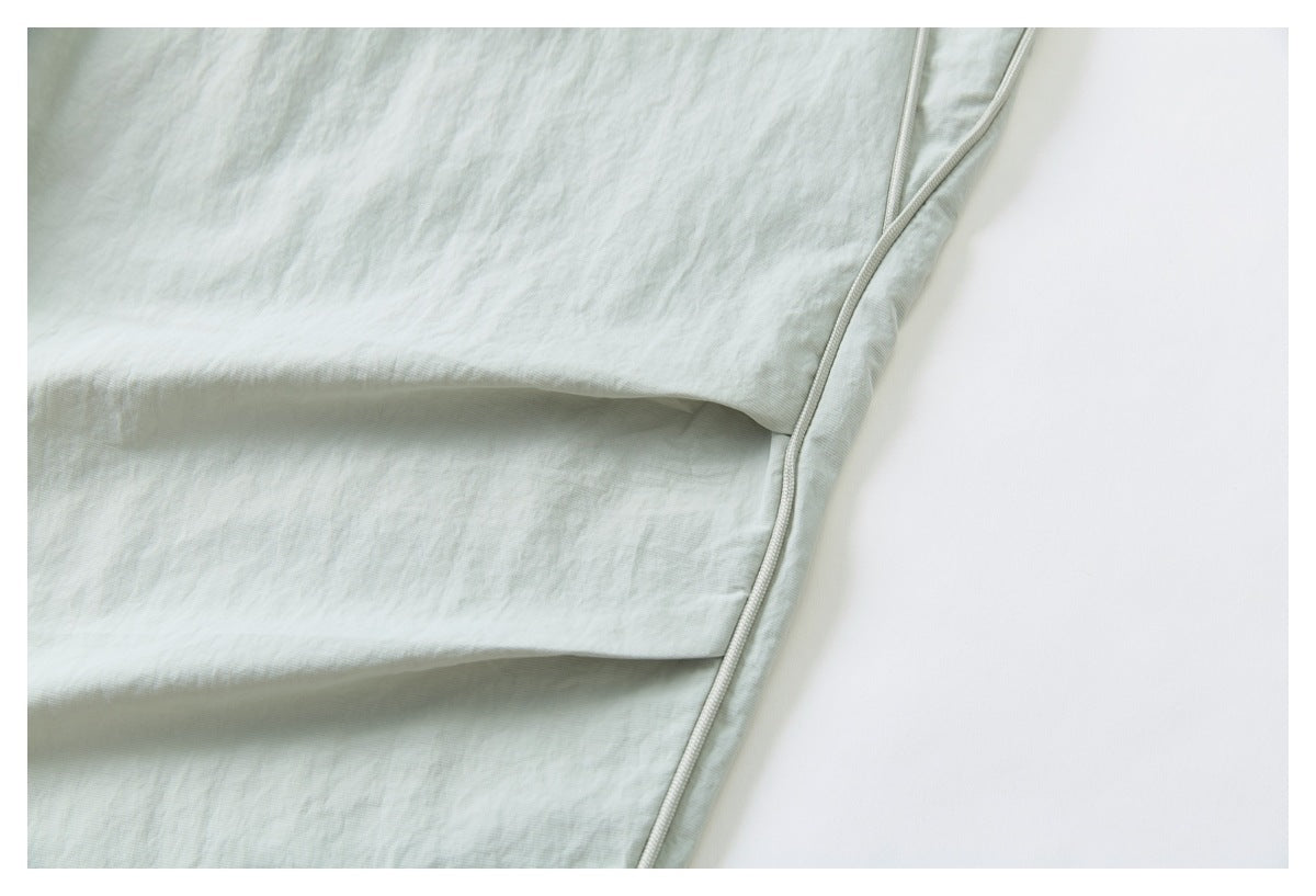 Close-up of the pale sage-gray pants fabric and curved piping along a folded section.