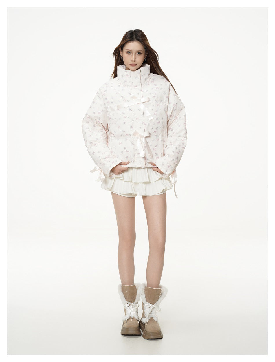 Model wearing a pale floral-print puffer jacket with ribbon ties, a white ruffled skirt, and tan fur-trimmed boots.