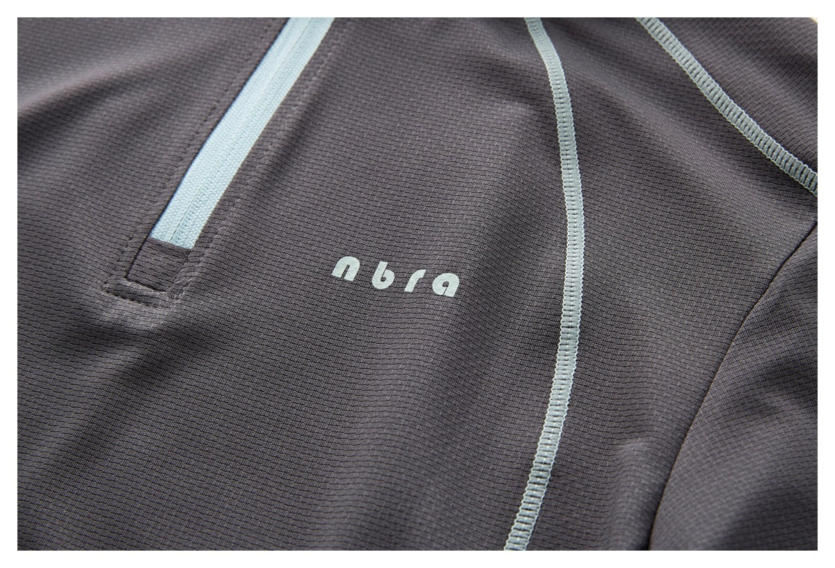 Close-up of a charcoal top's pale blue zipper trim, curved seams, and small chest lettering.