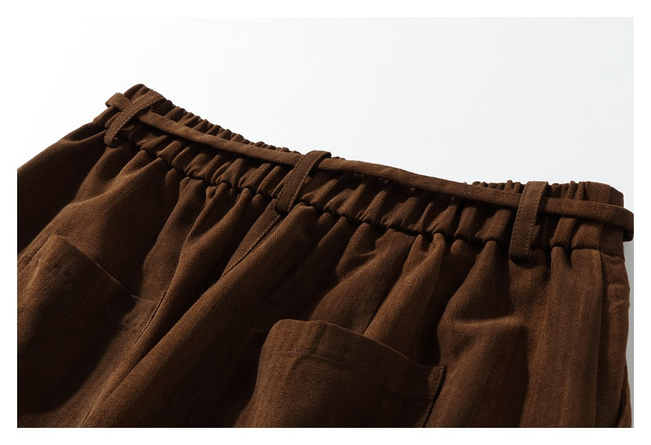 Close-up of dark brown trousers with an elastic waist, drawstring, belt loops and a front pocket.