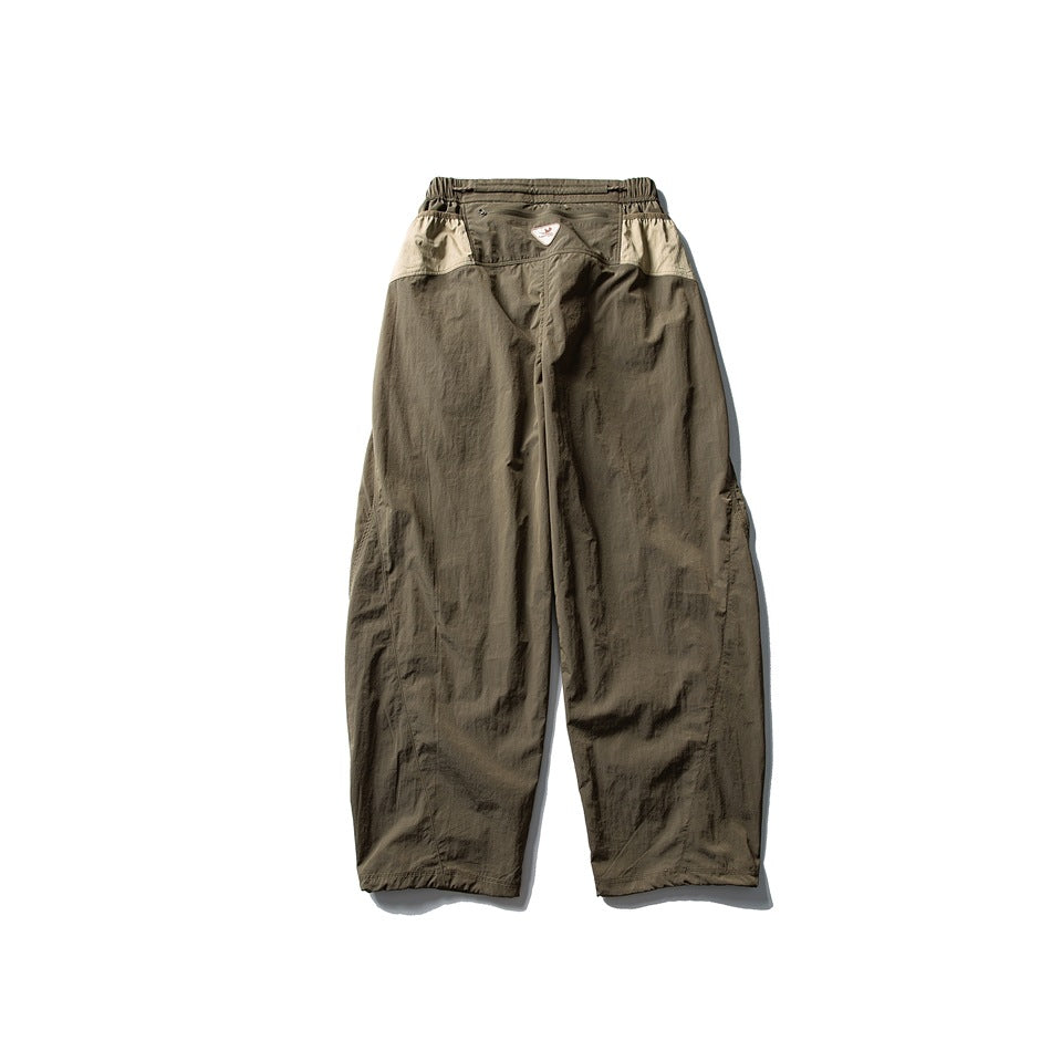 Back view of olive-brown wide-leg pants with a gathered waist and pale contrasting panels at the hips.