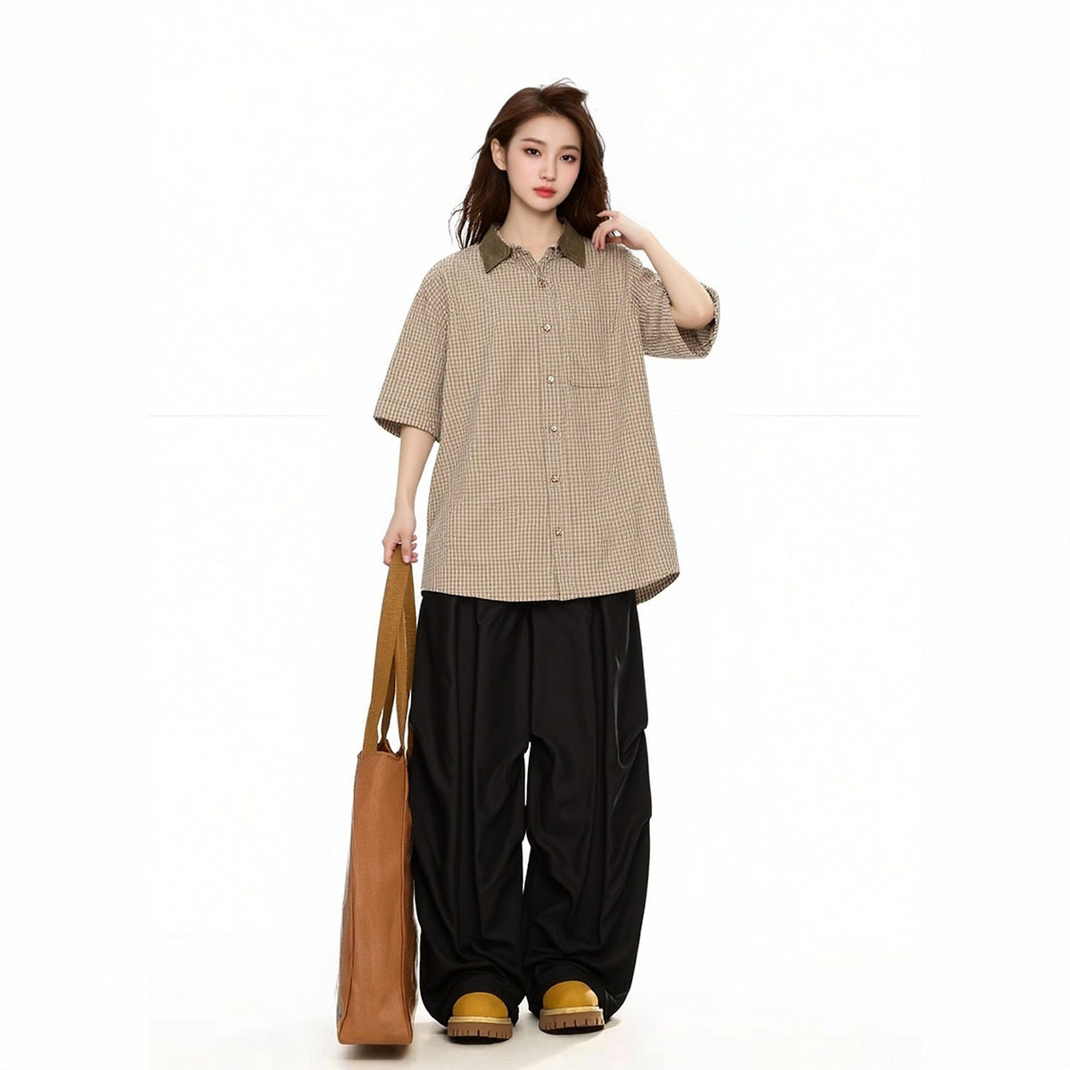 Model wearing a beige checked short-sleeve button-up shirt with a brown collar and black wide-leg pants.