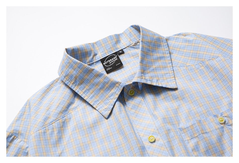 Close-up of a flat-laid light blue and beige plaid shirt's collar and upper button front.