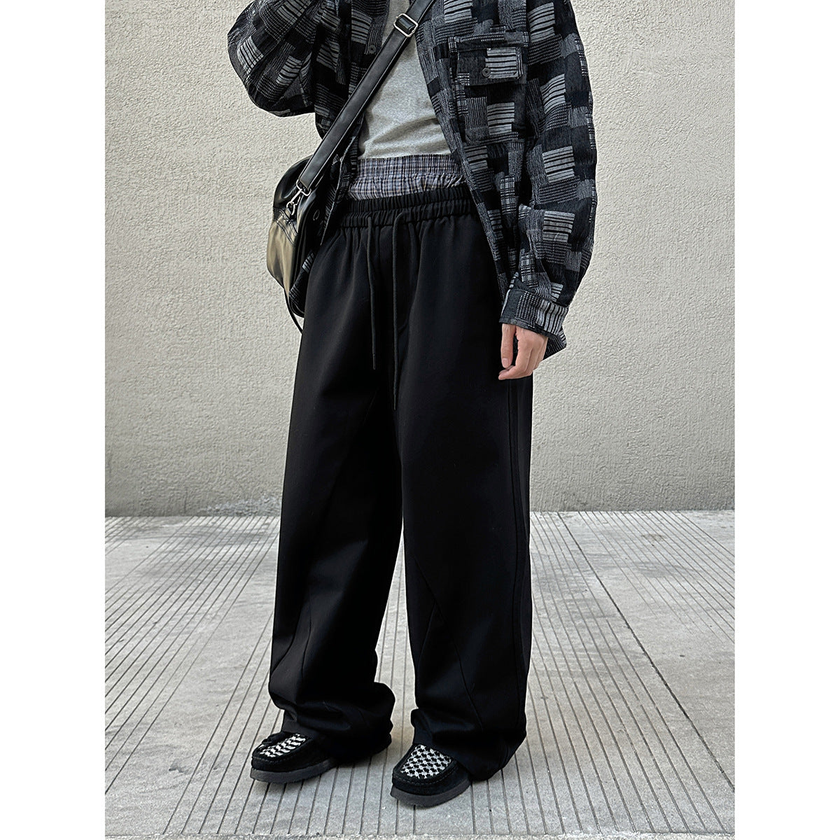 Model wearing black wide-leg drawstring trousers with a black-and-gray patterned overshirt.