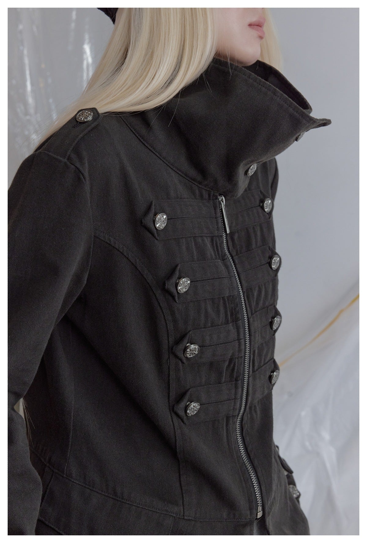 Close-up of a model wearing a black jacket with a tall collar, silver buttons, and a front zipper.