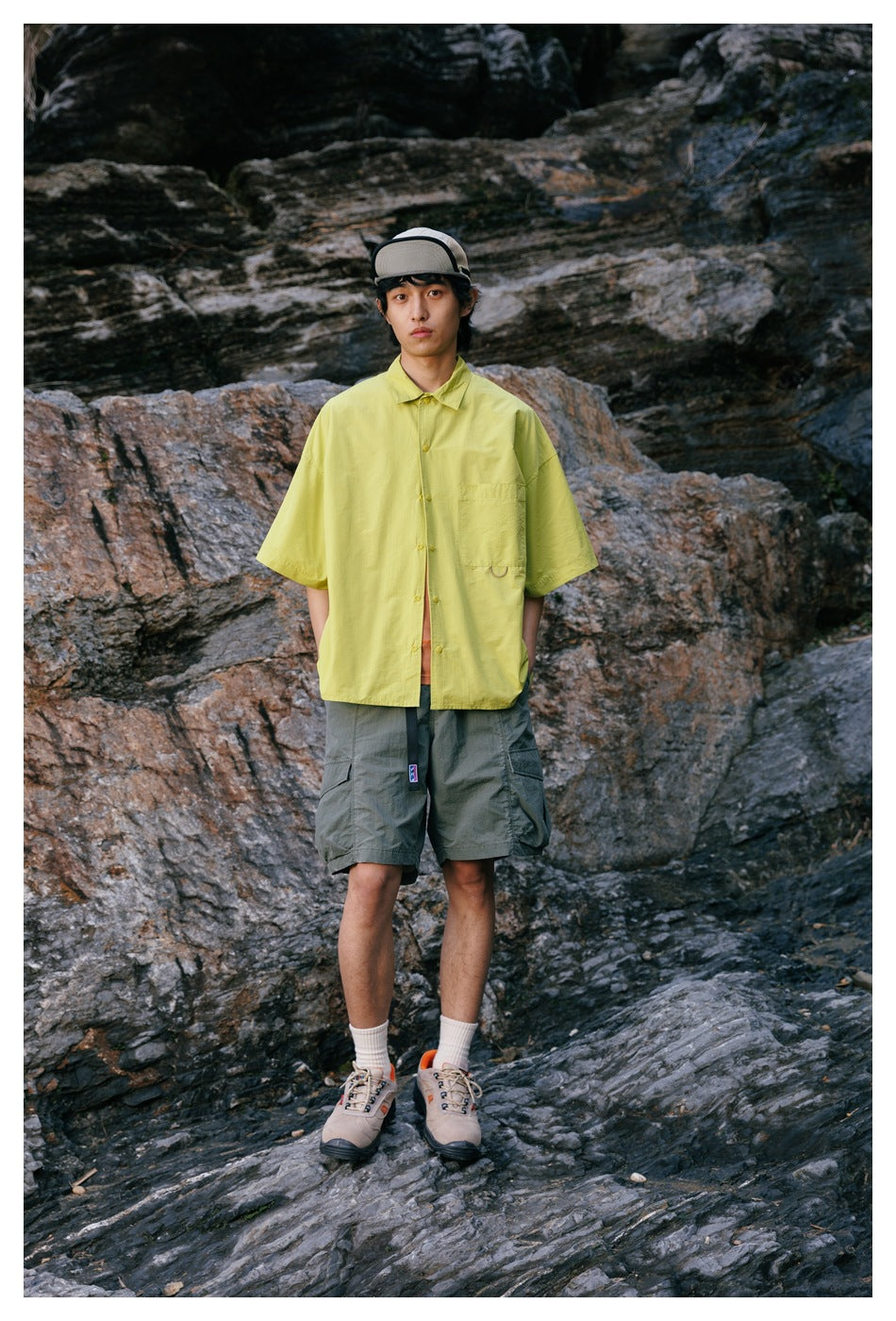 Model outdoors wearing a bright yellow-green short-sleeve button-up shirt with a chest pocket and gray cargo shorts.