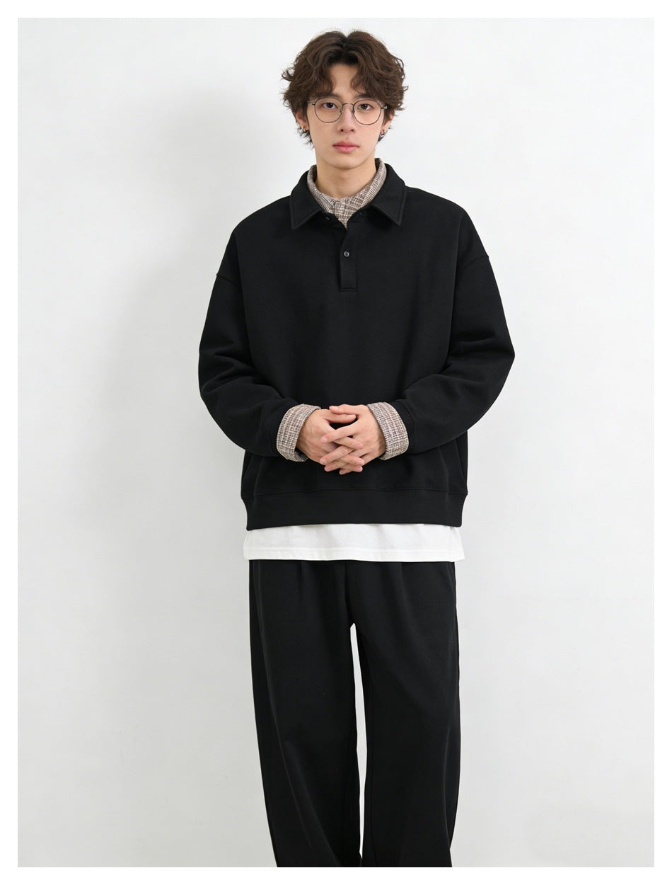 Front view of a model wearing a black collared pullover with checked shirt cuffs and collar.